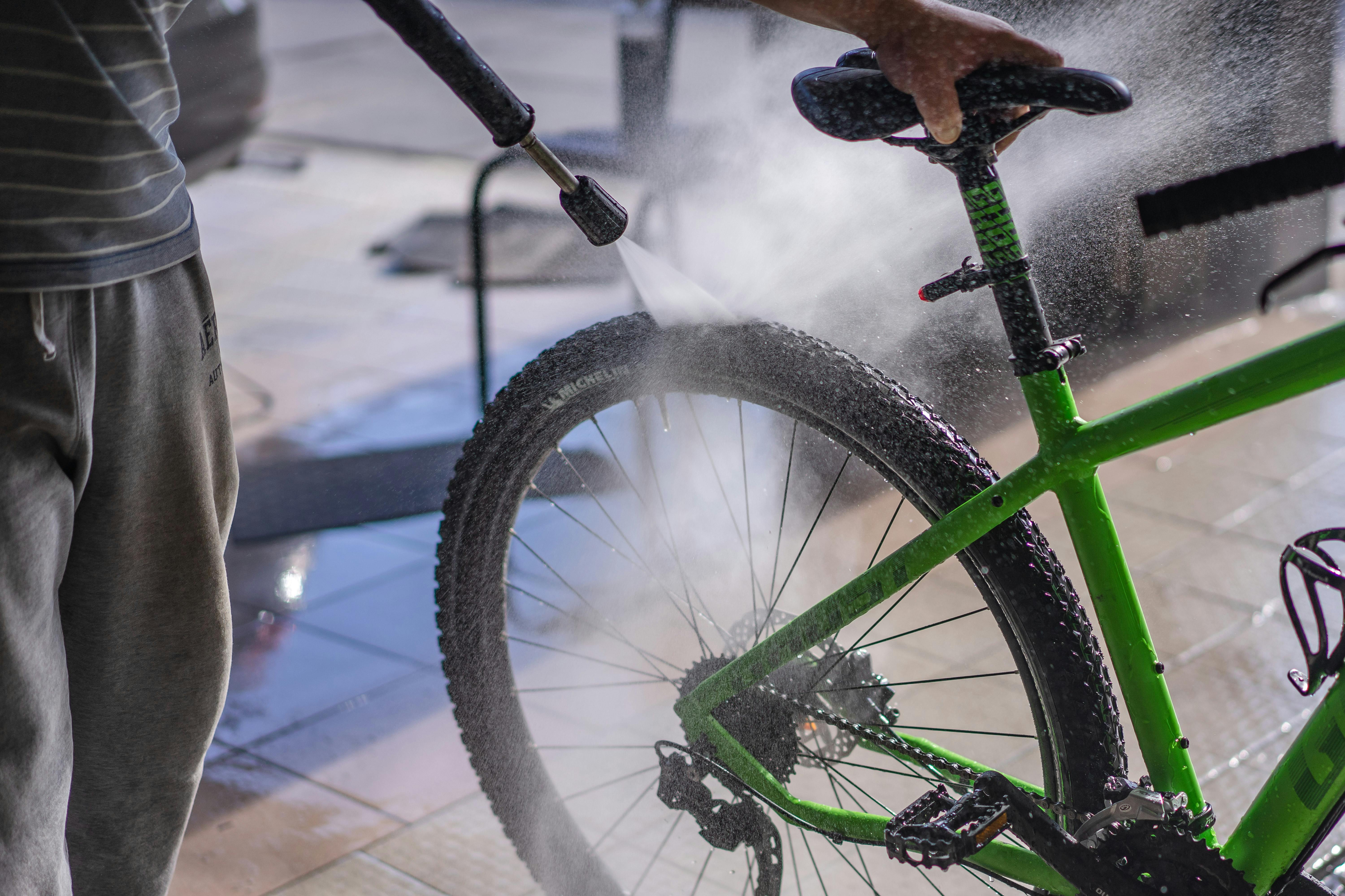Close-up of pressure washer cleaning green bicycle wheel and tire - high-pressure water spray removes dirt from spokes, rim, and rubber for bike maintenance