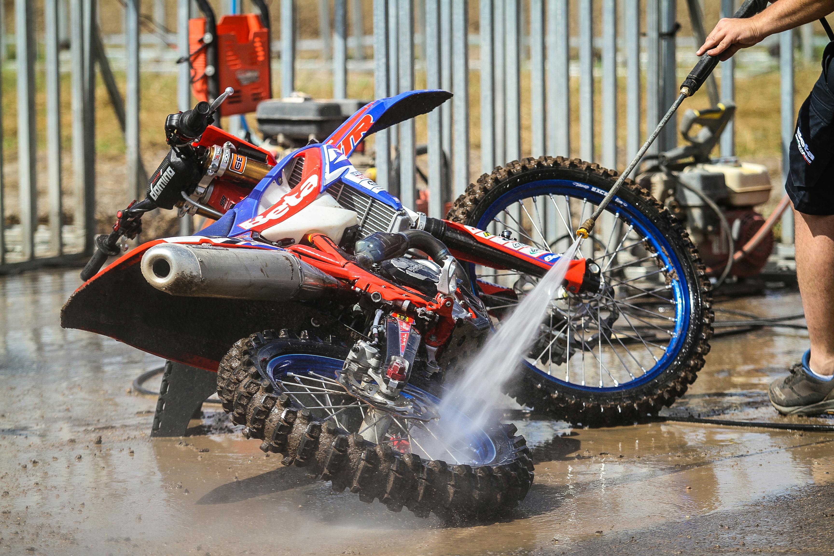 Professional pressure washing of red and blue dirt bike motocross motorcycle - high-pressure cleaning removes mud and grime from engine, frame, and wheels for vehicle maintenance